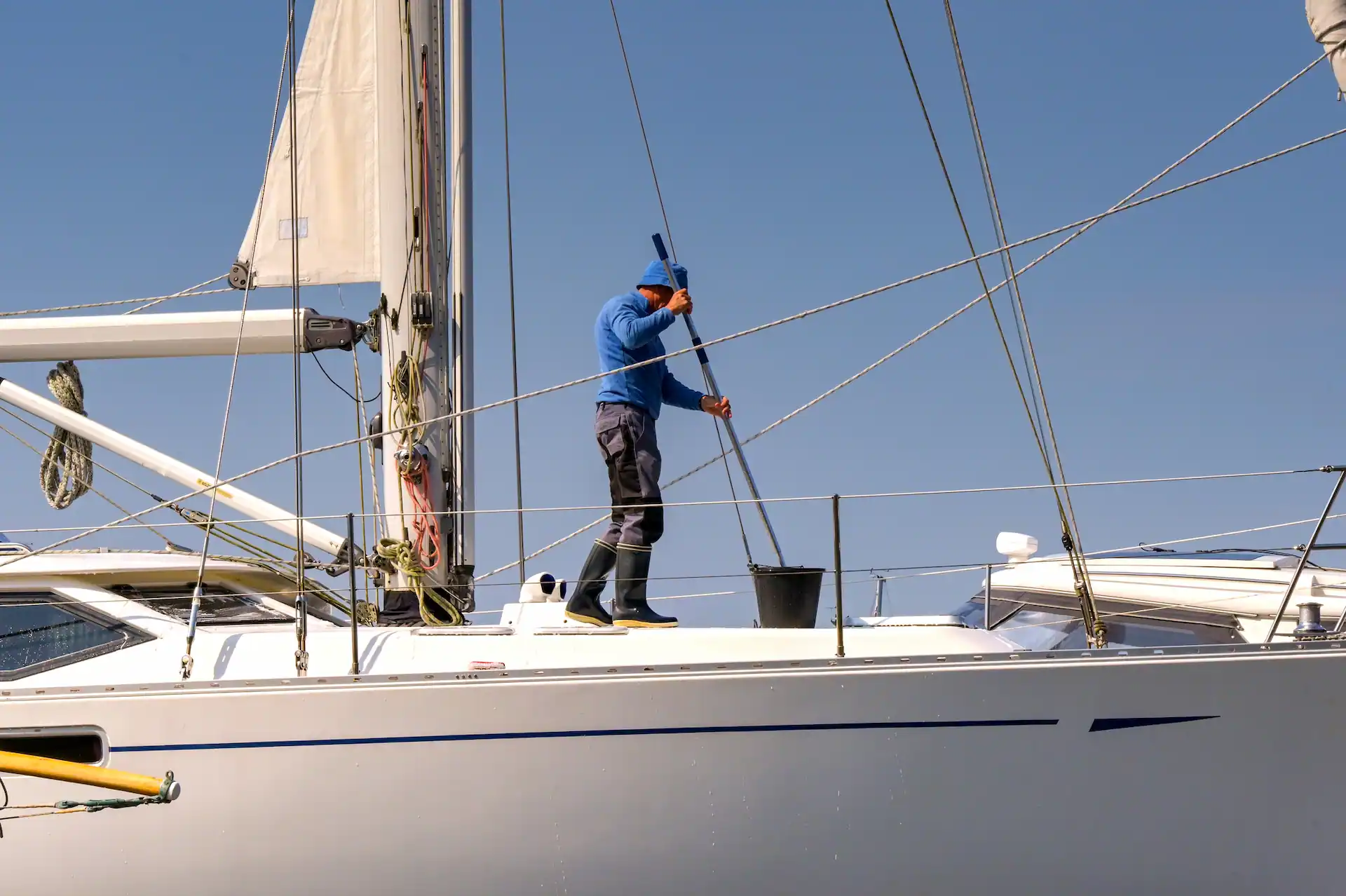 Person cleaning the deck of a yacht in a boatyard