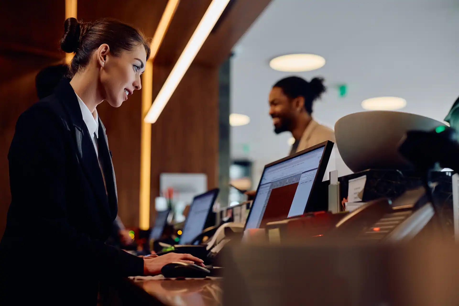 Smiling hotel manager working on a computer at reception desk
